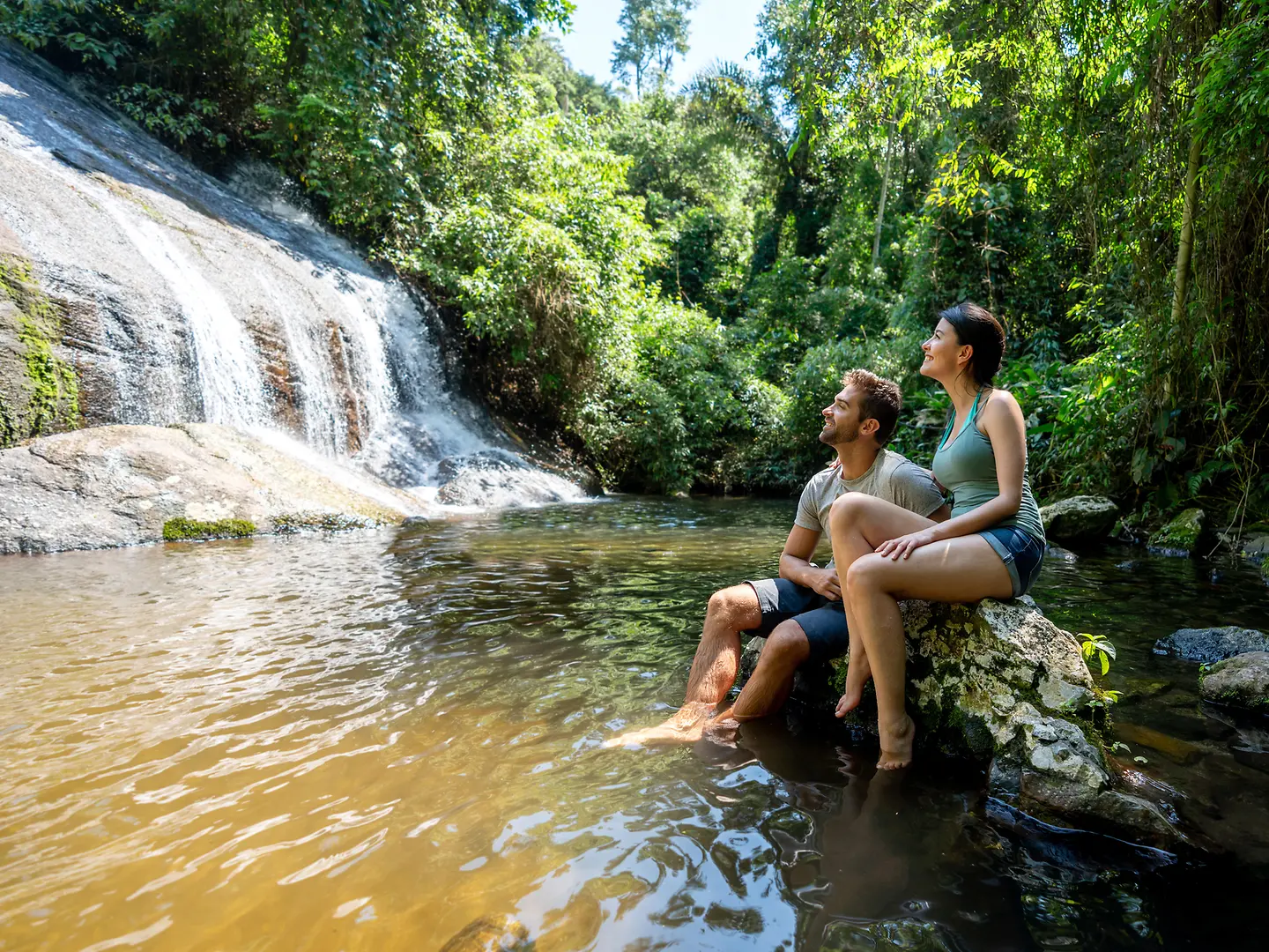 Ein junges Paar schaut im Urlaub auf einen Wasserfall. 