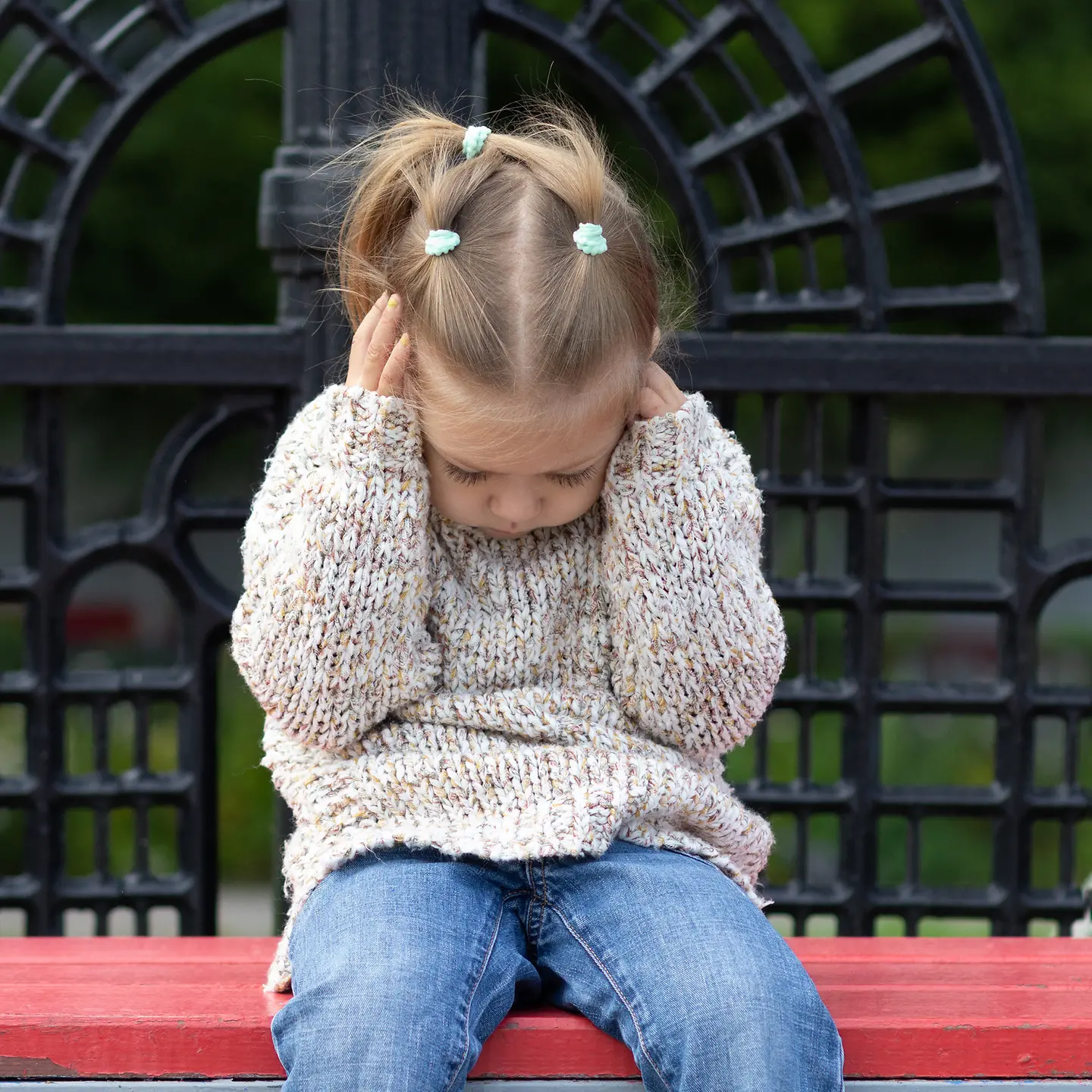 Ein kleines Mädchen sitzt auf einer Bank und hält sich die Ohren fest