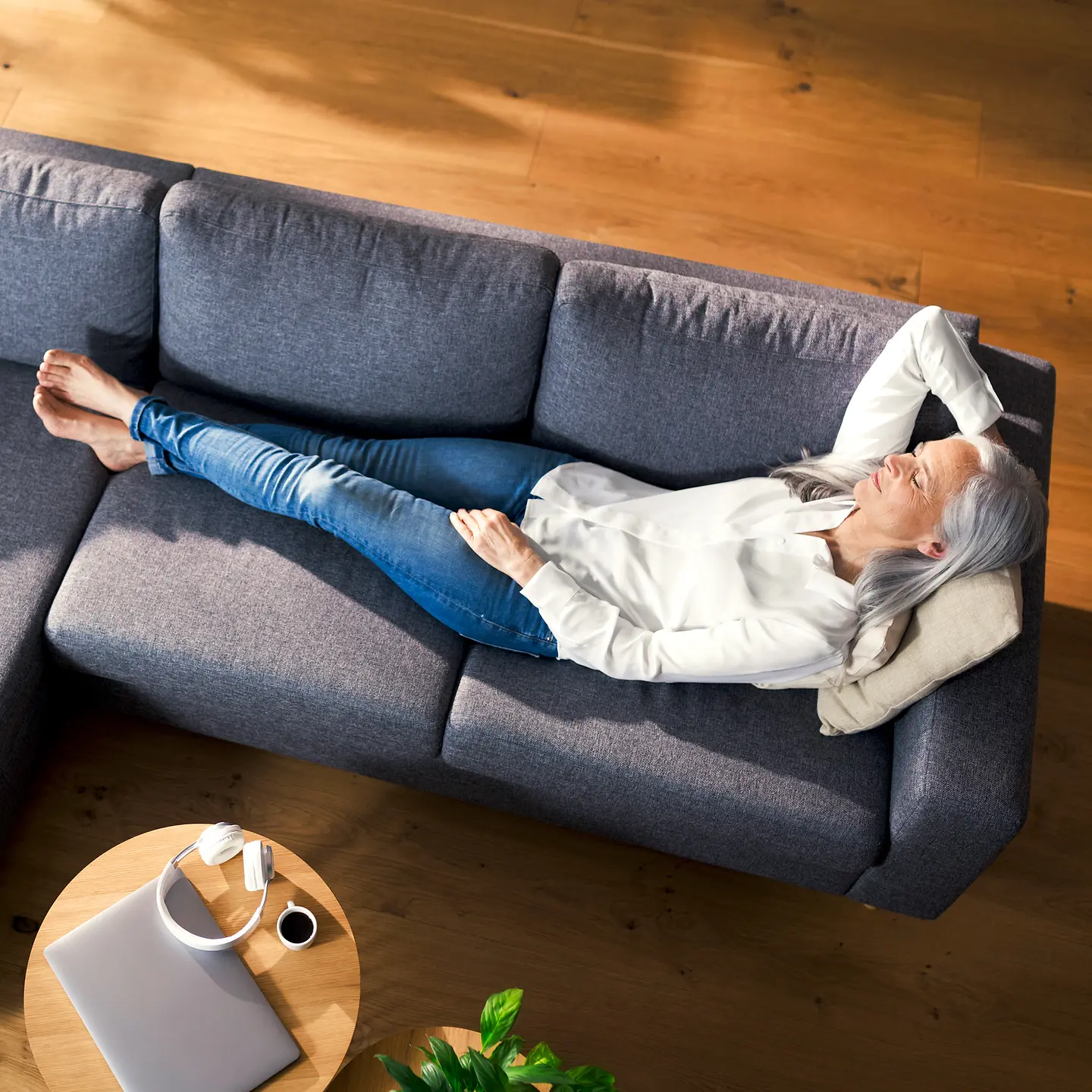 Eine Frau mit grauen Haaren liegt auf einem Sofa im Wohnzimmer und schläft