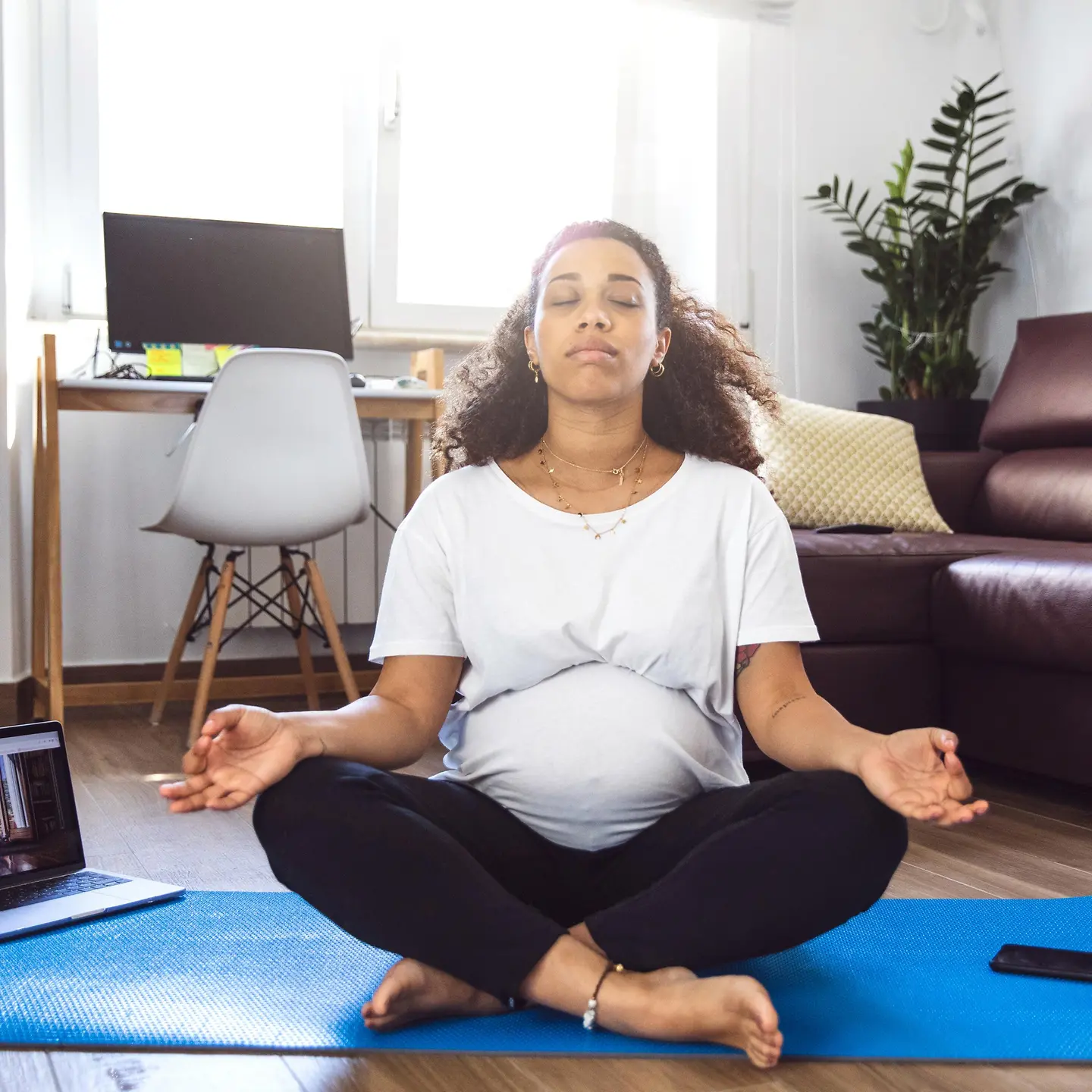 Eine Schwangere sitzt im Wohnzimmer und macht Yoga