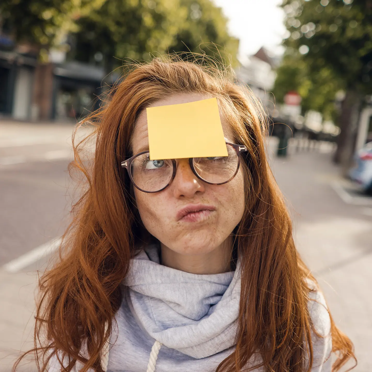 Eine junge Frau schaut skeptisch auf einen gelben Zettel, der auf ihrer Stirn klebt.