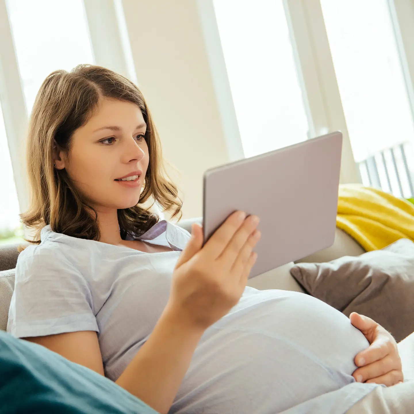Junge schwangere Frau mit Tablet auf einer Couch