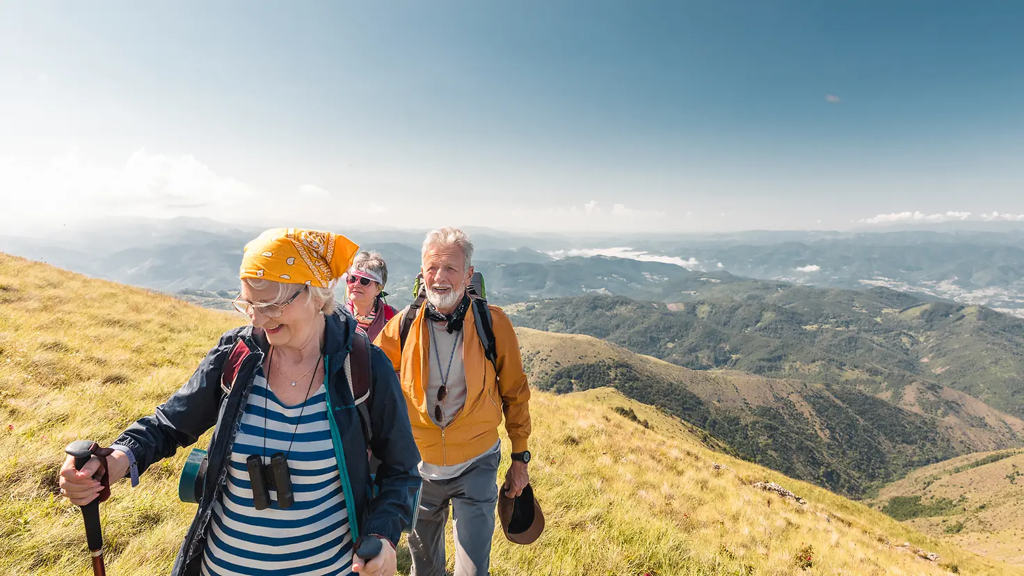 Eine Gruppe von drei Senioren, die zusammen in den Bergen wandern.