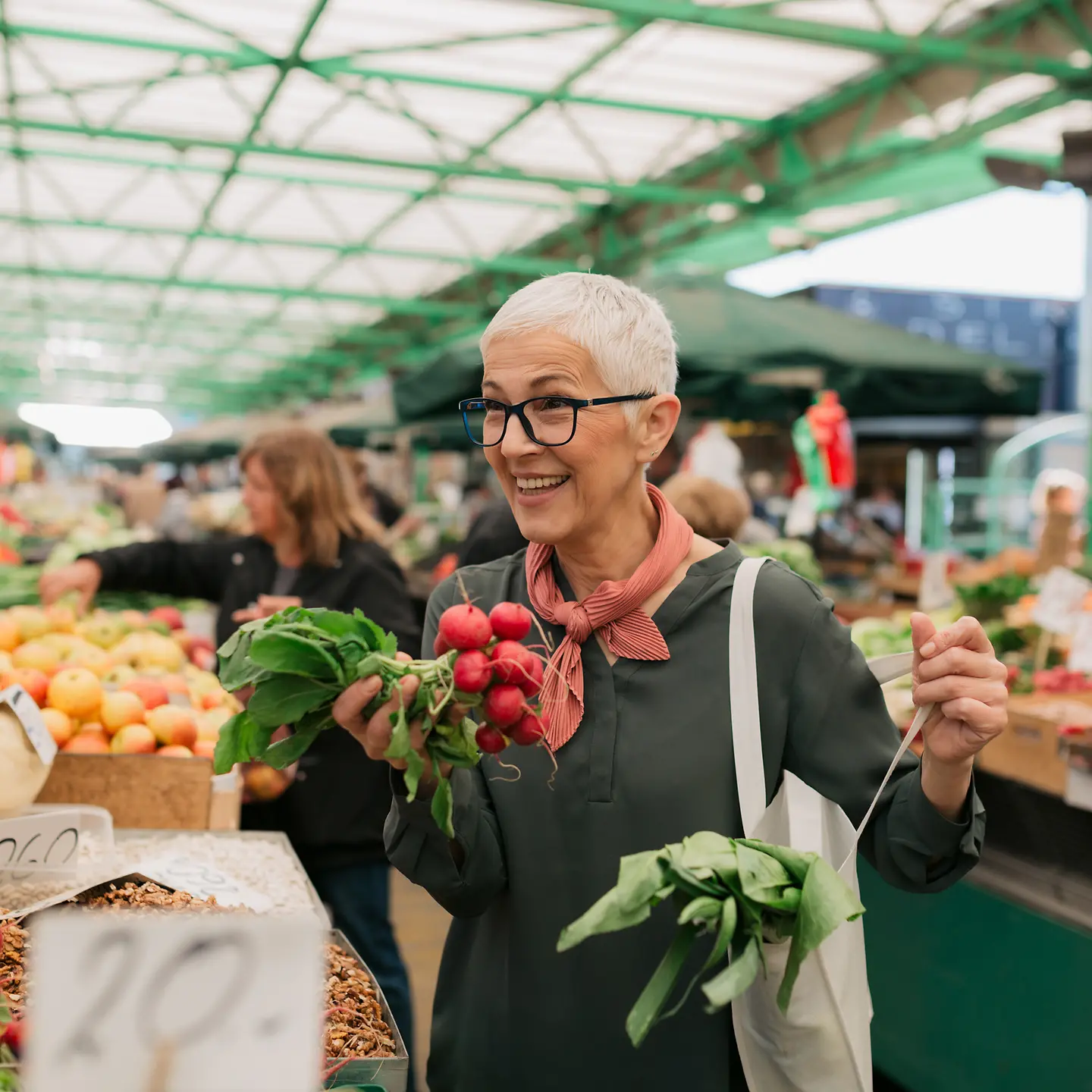 Lächelnde ältere Frau mit kurzen grauen Haaren kauft Lebensmittel auf dem Wochenmarkt ein