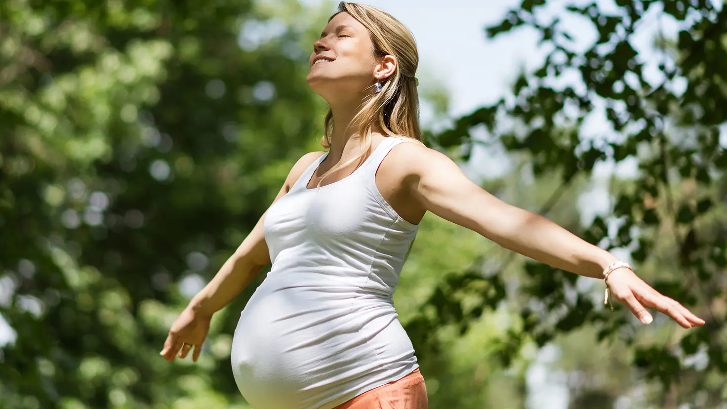 Schwangere Frau in der etwa 27. Schwangerschaftswoche genießt die Sonne mit geschlossen Augen
