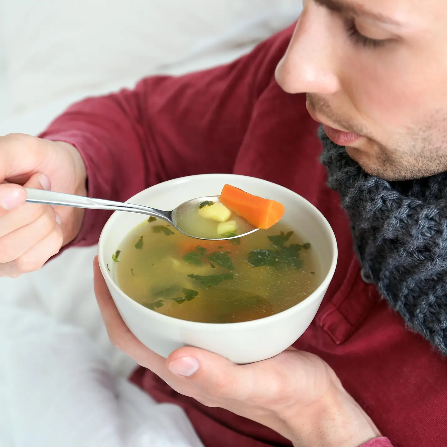 Ein Mann mit Schaal um den Hals isst eine warme Suppe