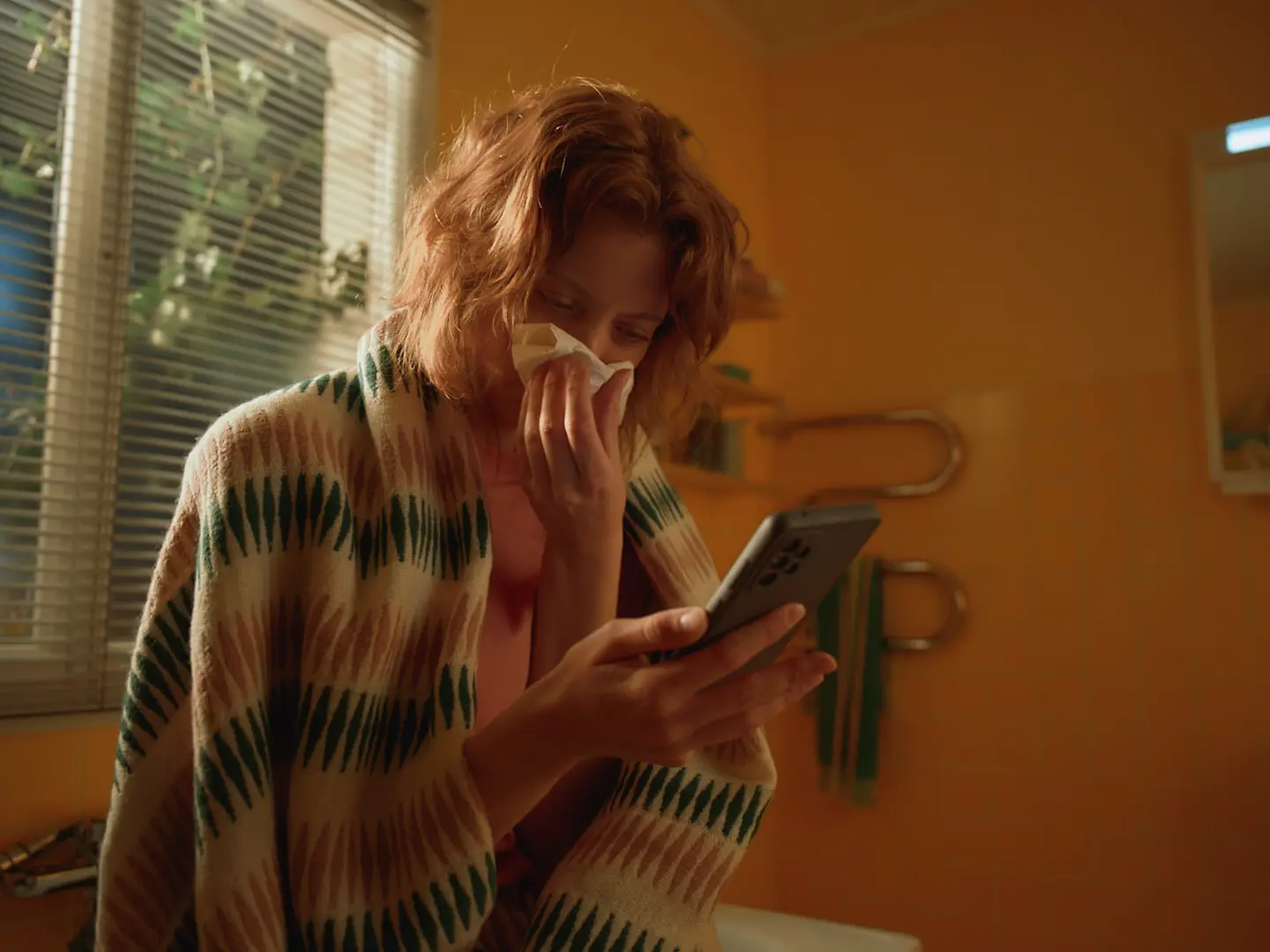 Eine junge Frau niest in ihr Taschentuch und nutzt die Teledoktor-App. 
