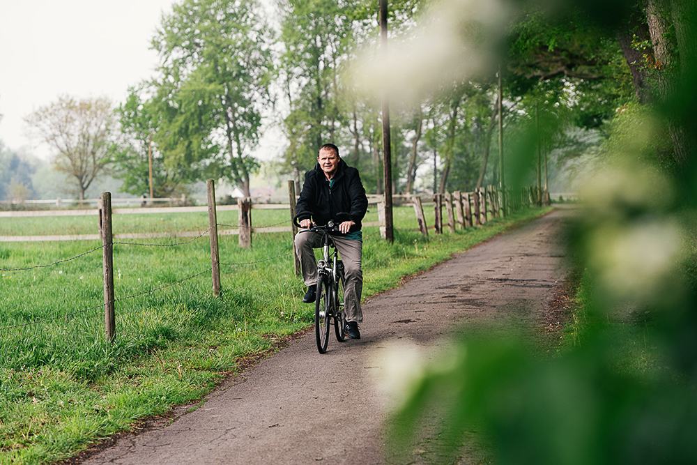Andreas Boelssen fährt mit dem Fahrrad auf einem Feldweg an Bäumen vorbei
