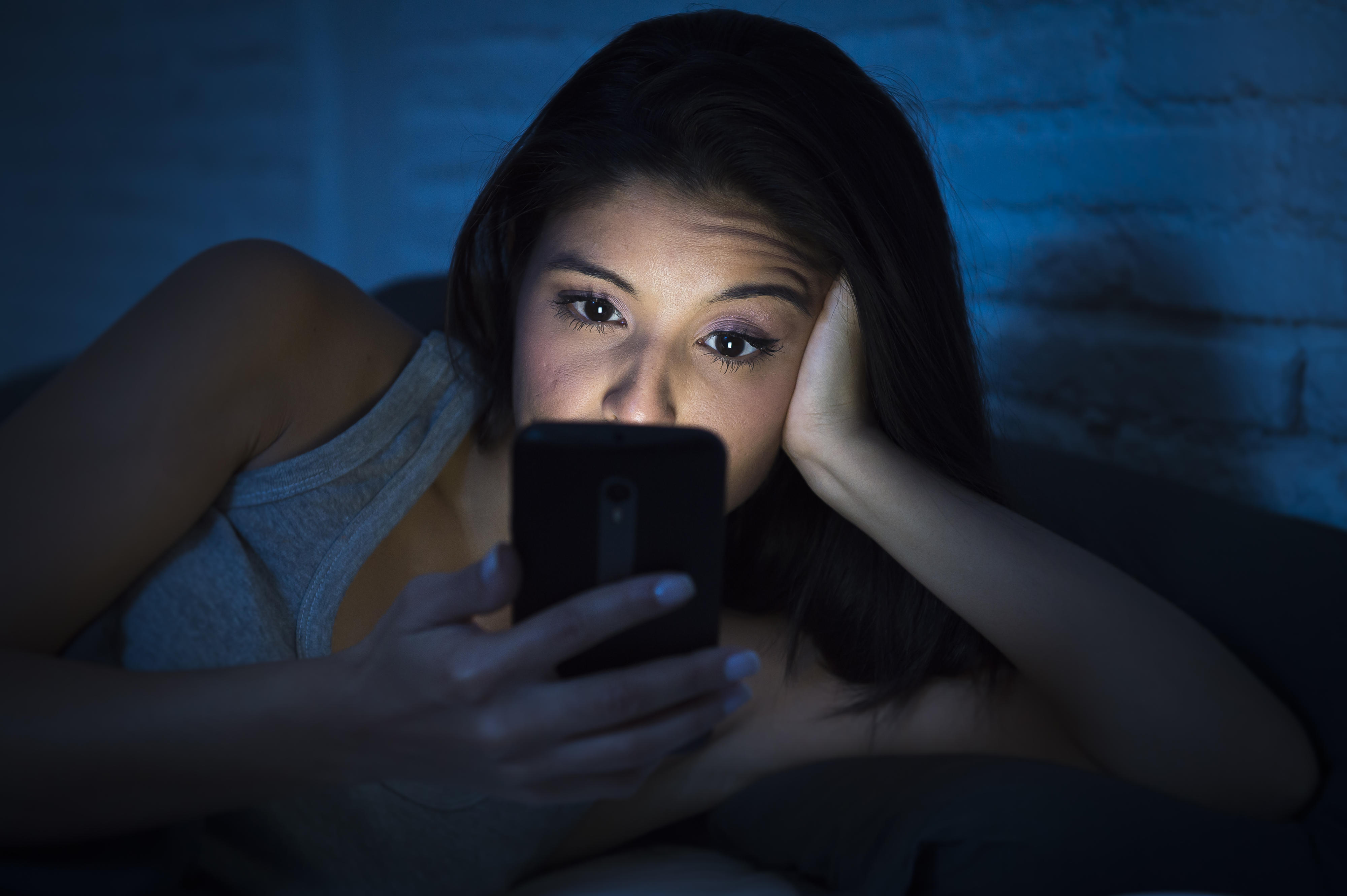 Eine Frau liegt im Dunklen im Bett und schaut auf ein Smartphone.