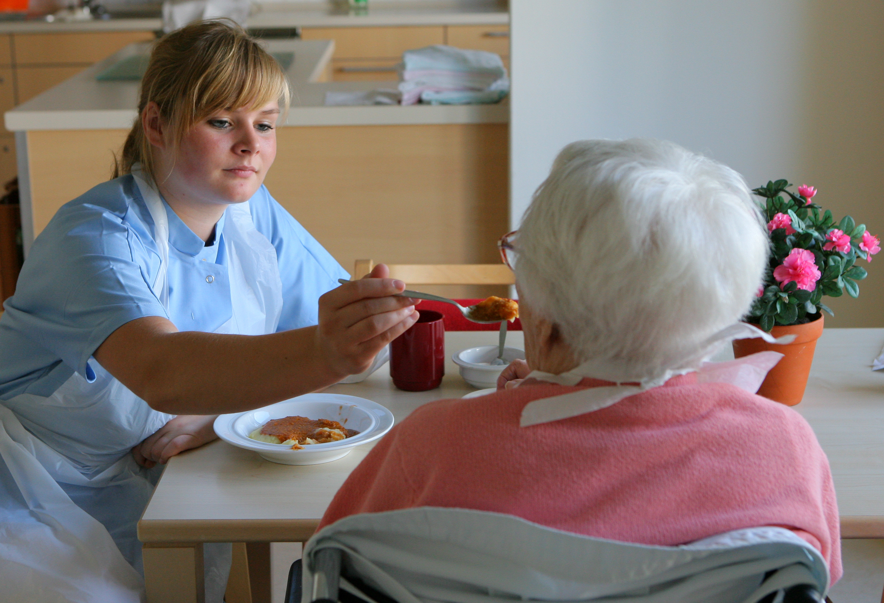 Pflege zu Hause: Pflegerin gibt Pflegebedürftiger zu essen