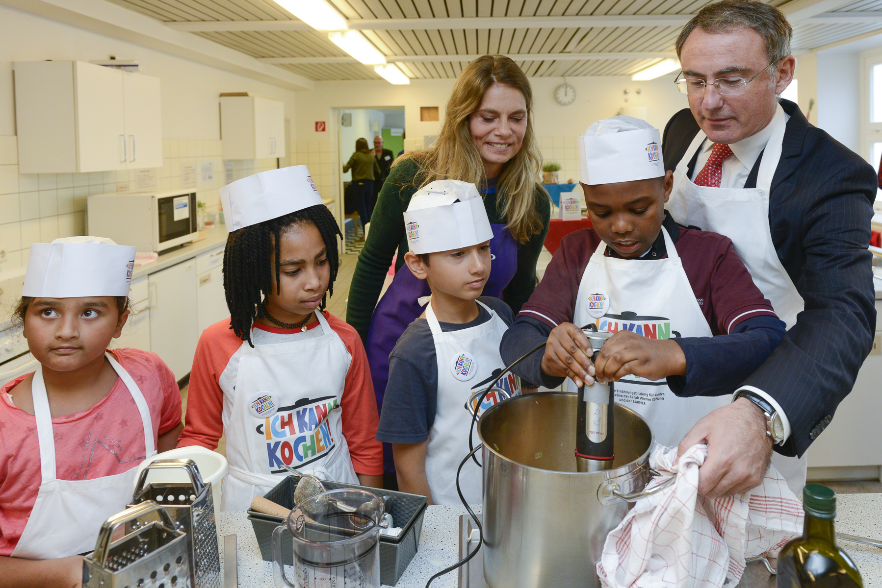 Sarah Wiener und Prof. Dr. Christoph Straub, Vorstandsvorsitzender der Barmer, kochen gemeinsam mit Kindern