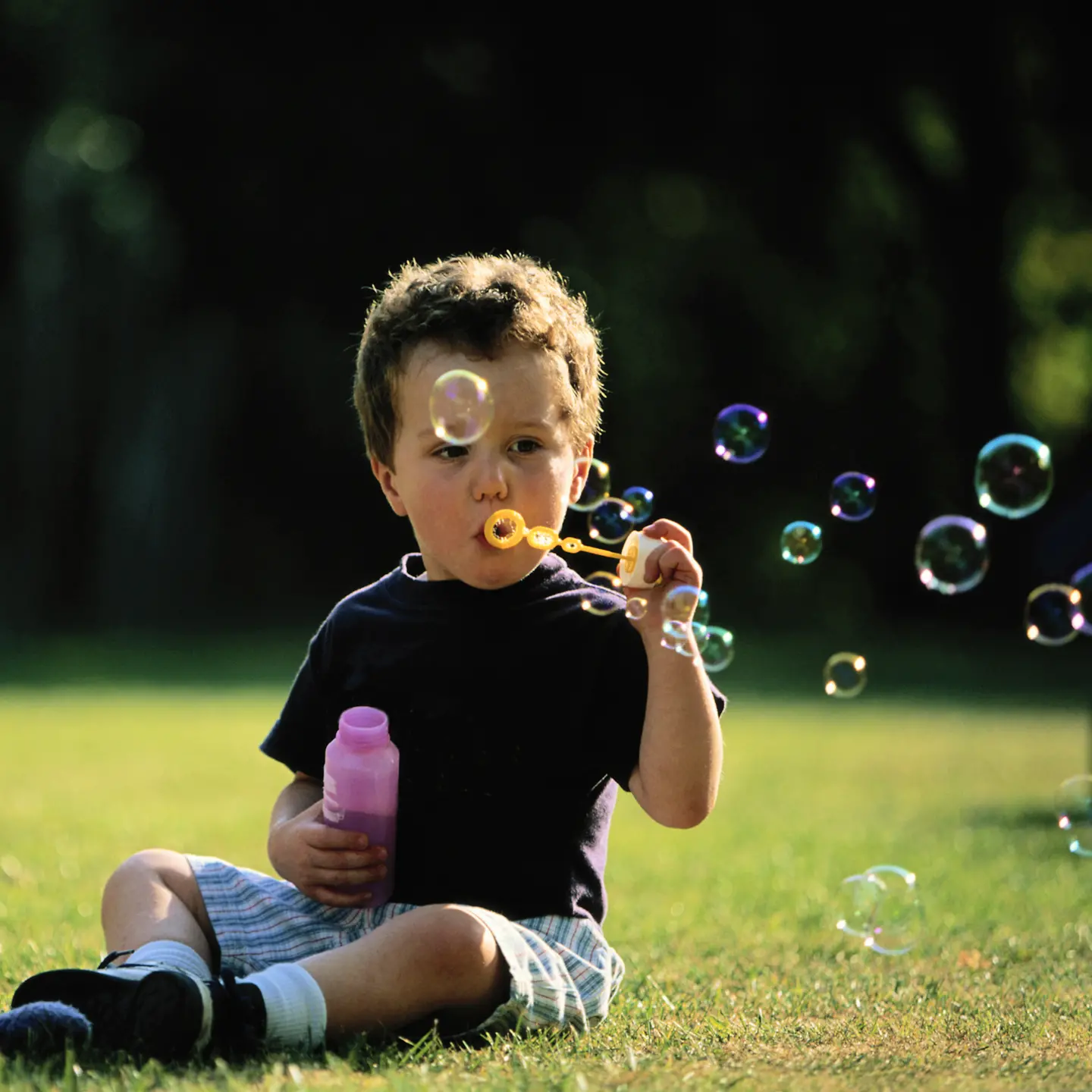 Ein Kleinkind sitzt auf der Wiese und bläst Seifenblasen