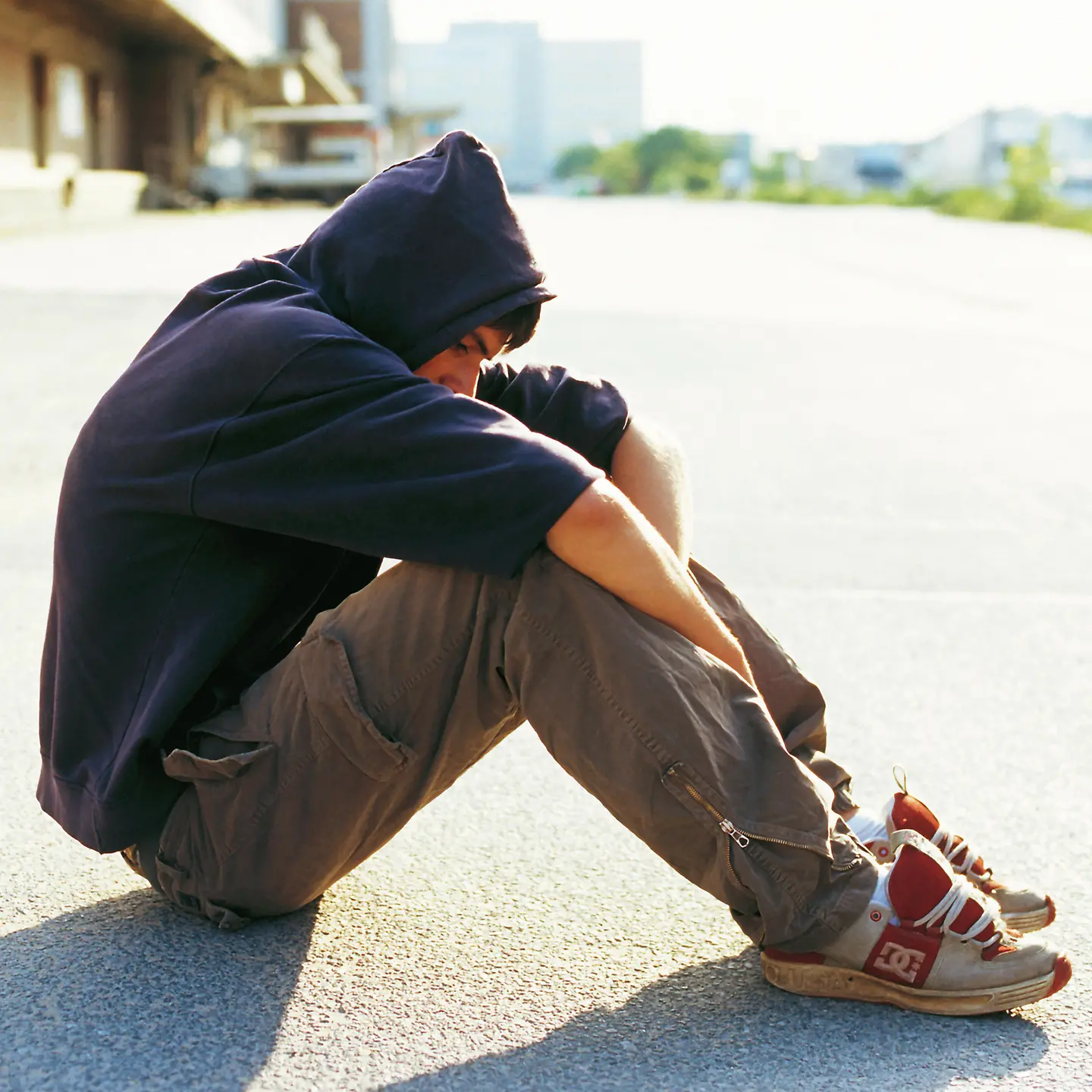Ein junger Mann sitzt mit Kapuzenpulli auf der Straße.