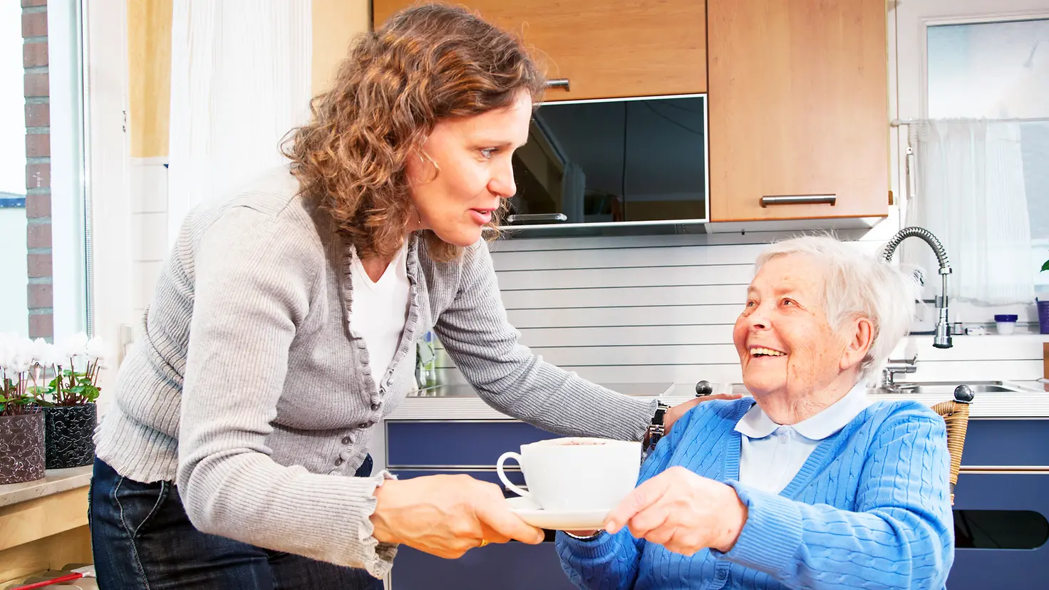 Eine pflegende Angehörige gibt einer Seniorin eine Tasse