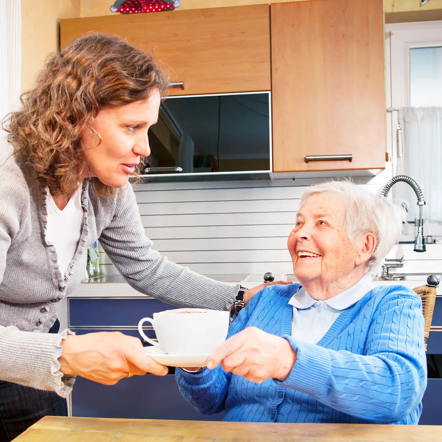Eine pflegende Angehörige gibt einer Seniorin eine Tasse