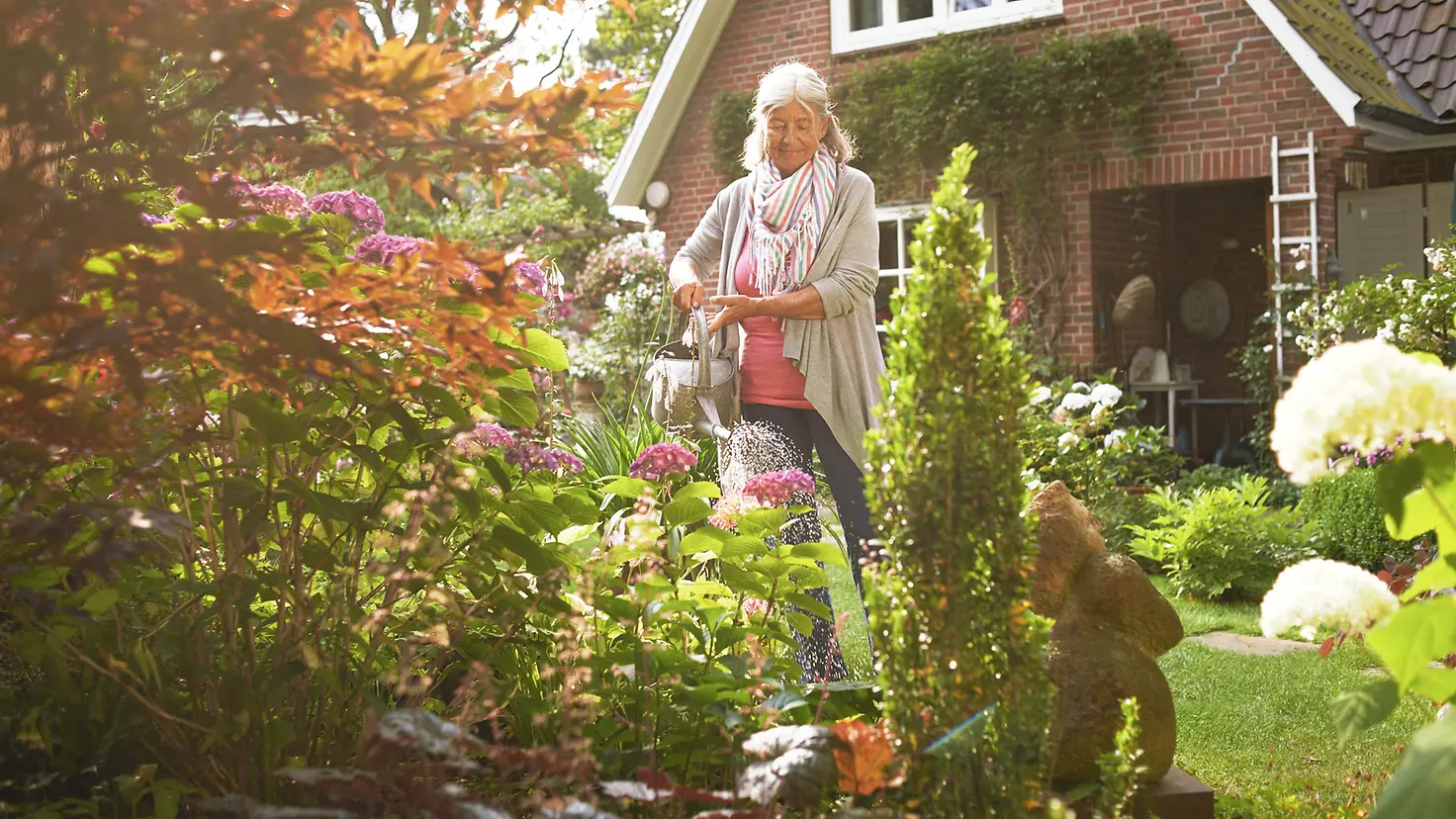 Eine ältere Frau gießt die Blumen vor ihrem Haus