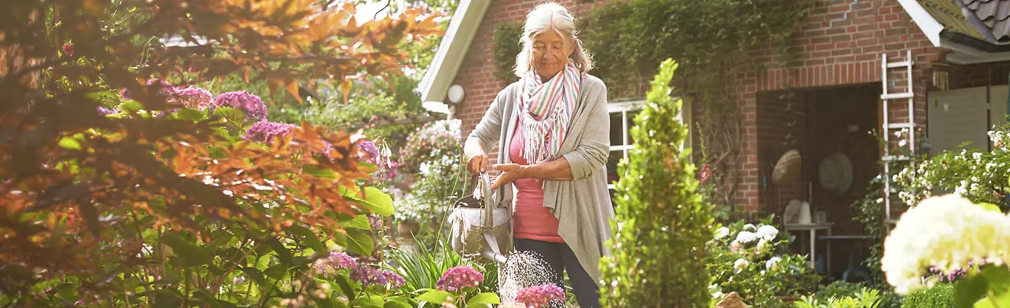 Eine ältere Frau gießt die Blumen vor ihrem Haus