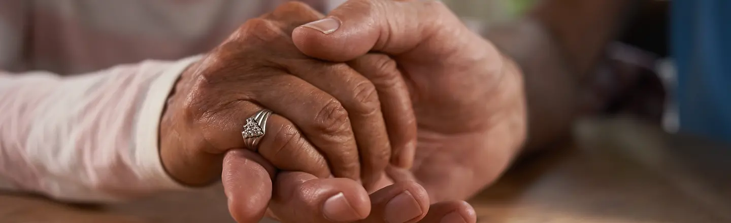 Ein älterer Mann hält die Hand seiner Frau