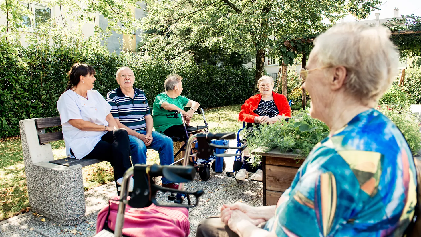 Eine Gruppe von Senioren sitzt im Garten und unterhält sich.