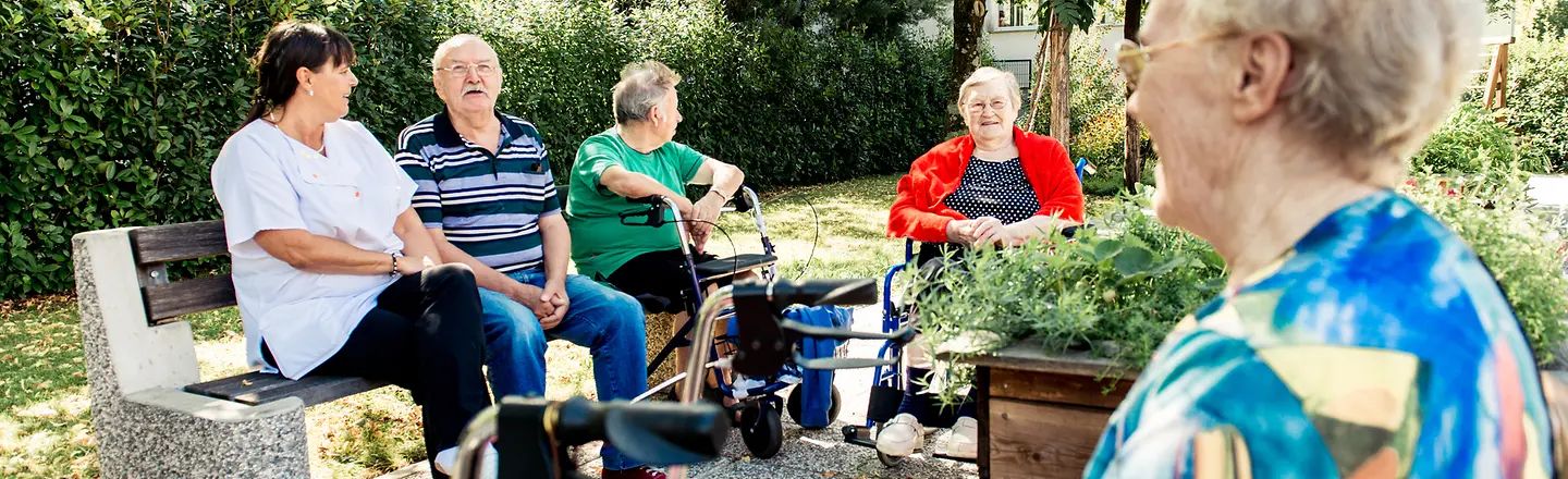Eine Gruppe von Senioren sitzt im Garten und unterhält sich.
