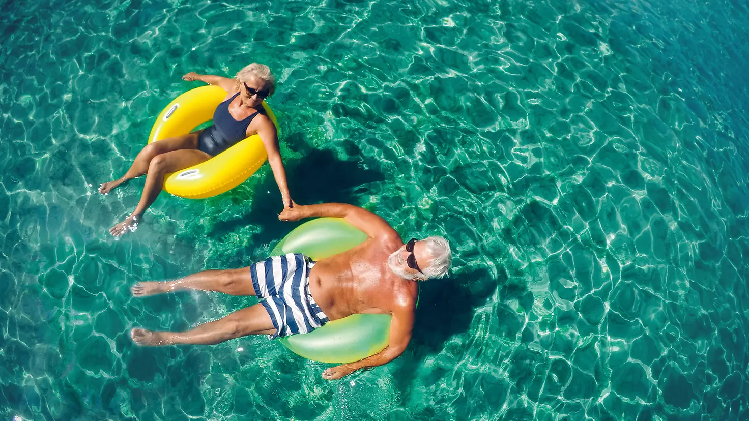 Zwei ältere Menschen liegen auf Schwimmreifen im Wasser