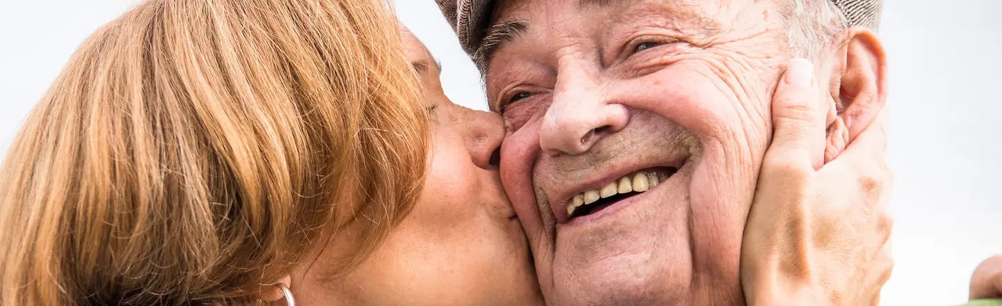 Eine Frau küsst einen alten Mann auf die Wange