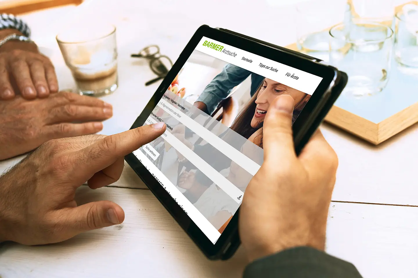 Ein Tablet mit Händen, auf dem die Arztsuche demonstriert wird.