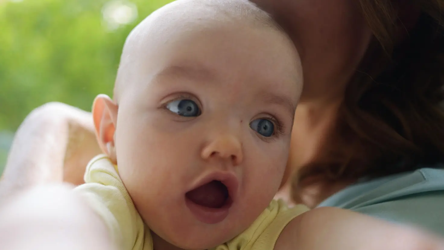 Ein Baby schaut mit offenem Mund über die Schulter einer Frau.