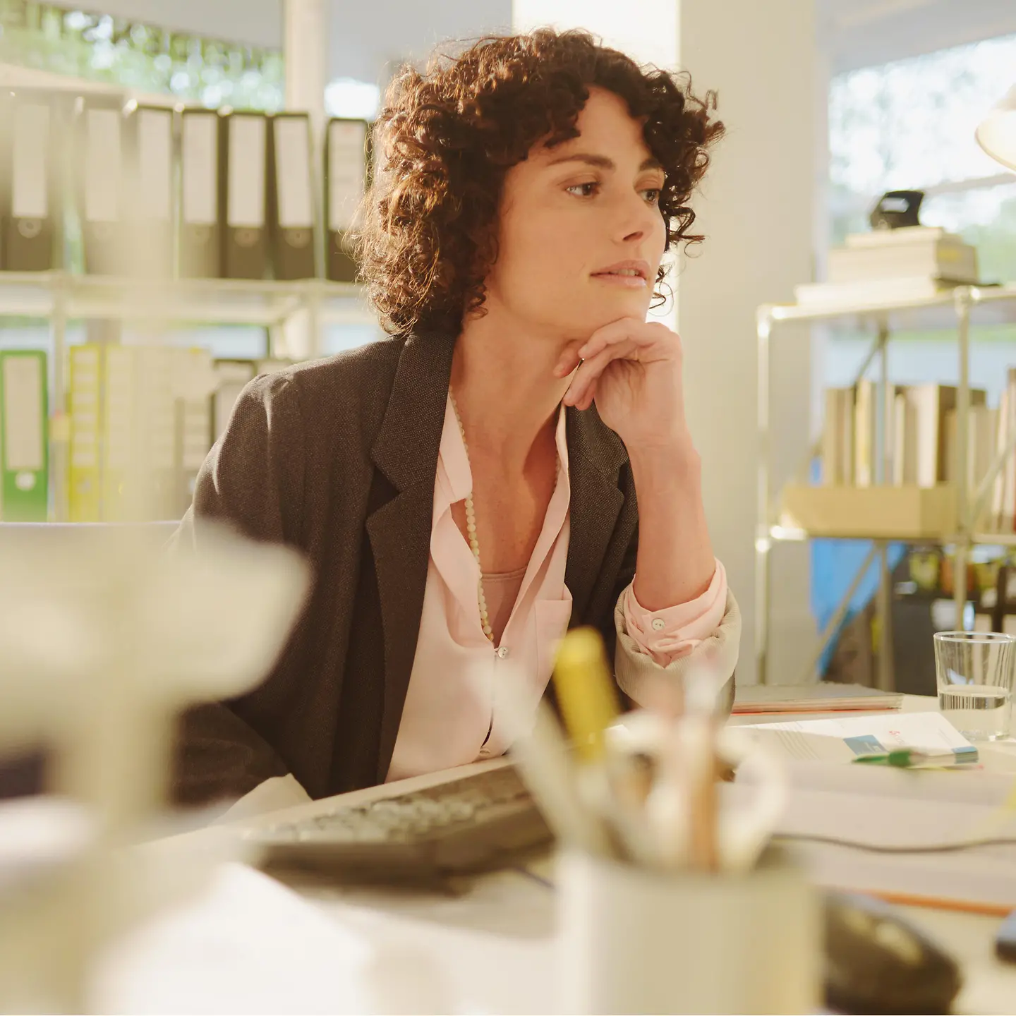 Eine Frau sitzt an ihrem Schreibtisch und denkt nach