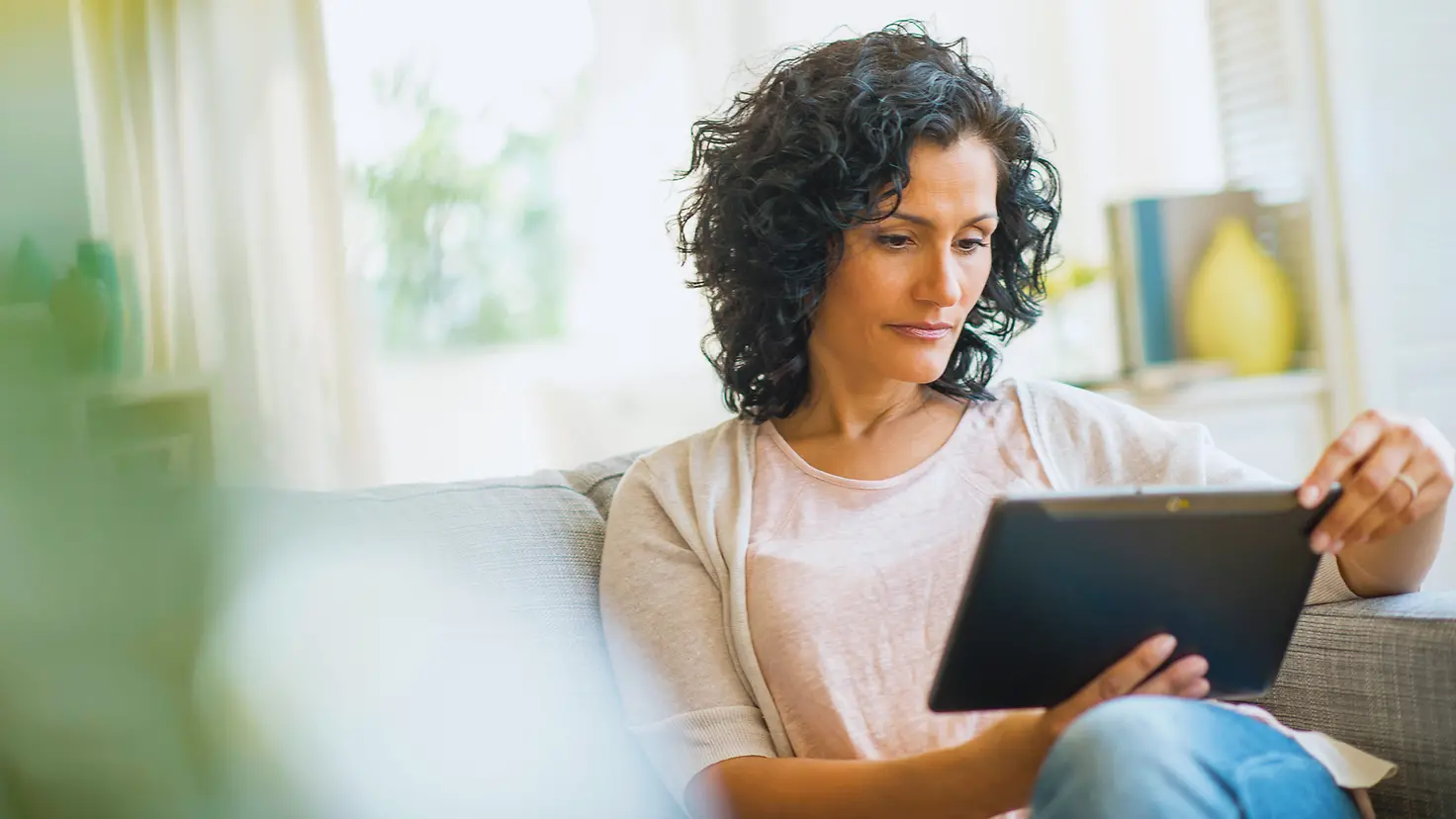 Eine Frau sitzt mit einem Tablet auf einer Couch