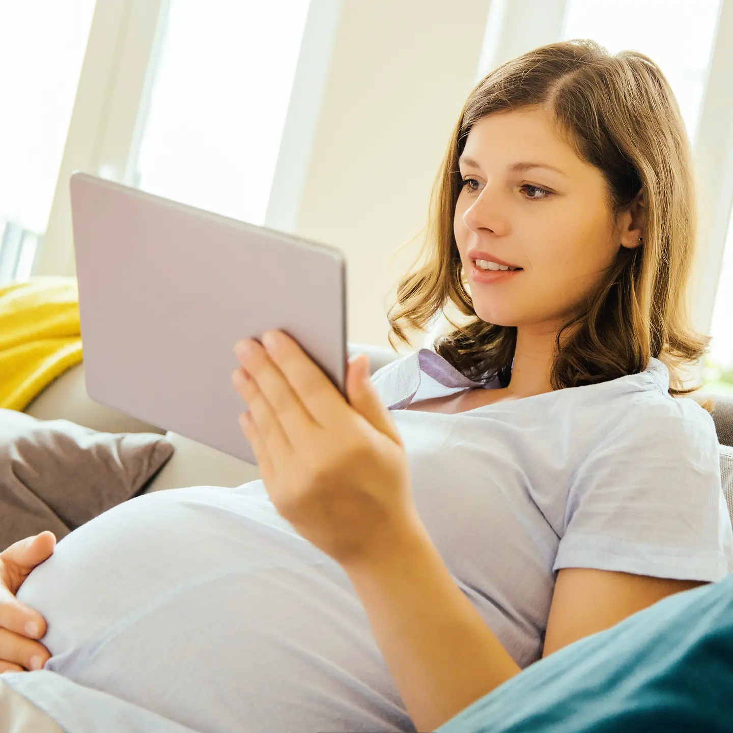 Eine schwangere Frau sitzt mit einem Tablet auf dem Sofa