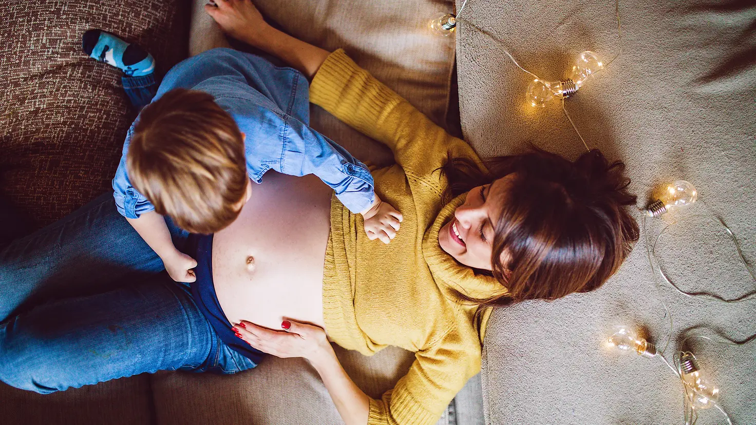 Eine schwangere Frau mit kleinem Kind liegt auf dem Boden