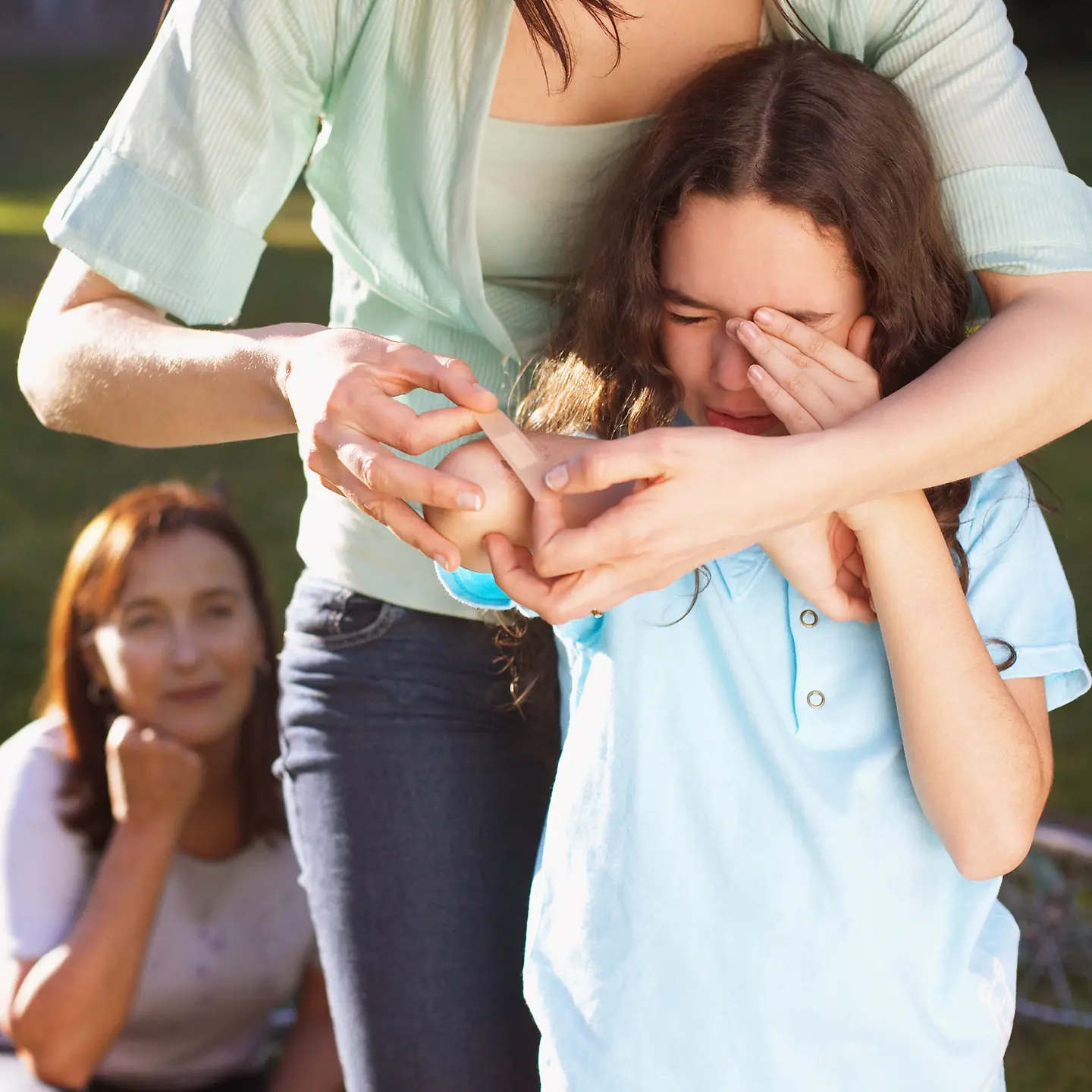 Ein weinendes Mädchen bekommt ein Pflaster auf den Ellenbogen geklebt