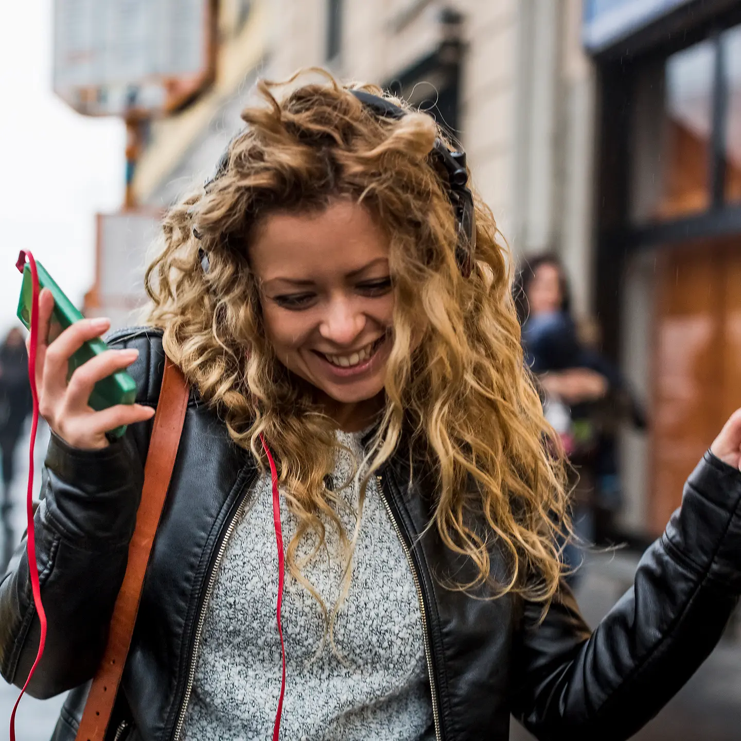 Eine junge Frau tanzt auf der Straße zur Musik aus ihrem Smartphone