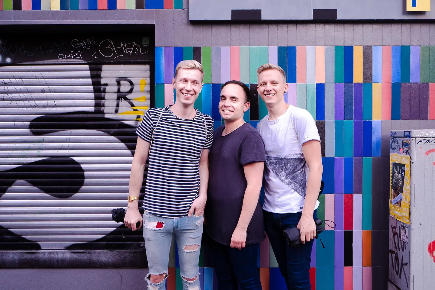 Drei junge Männer stehen vor einer bunten Wand