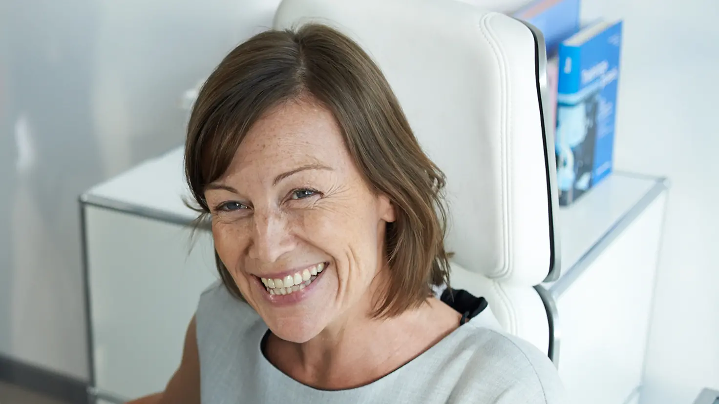 Eine Frau sitzt auf einem weißen Stuhl und schaut lachend Richtung Kamera