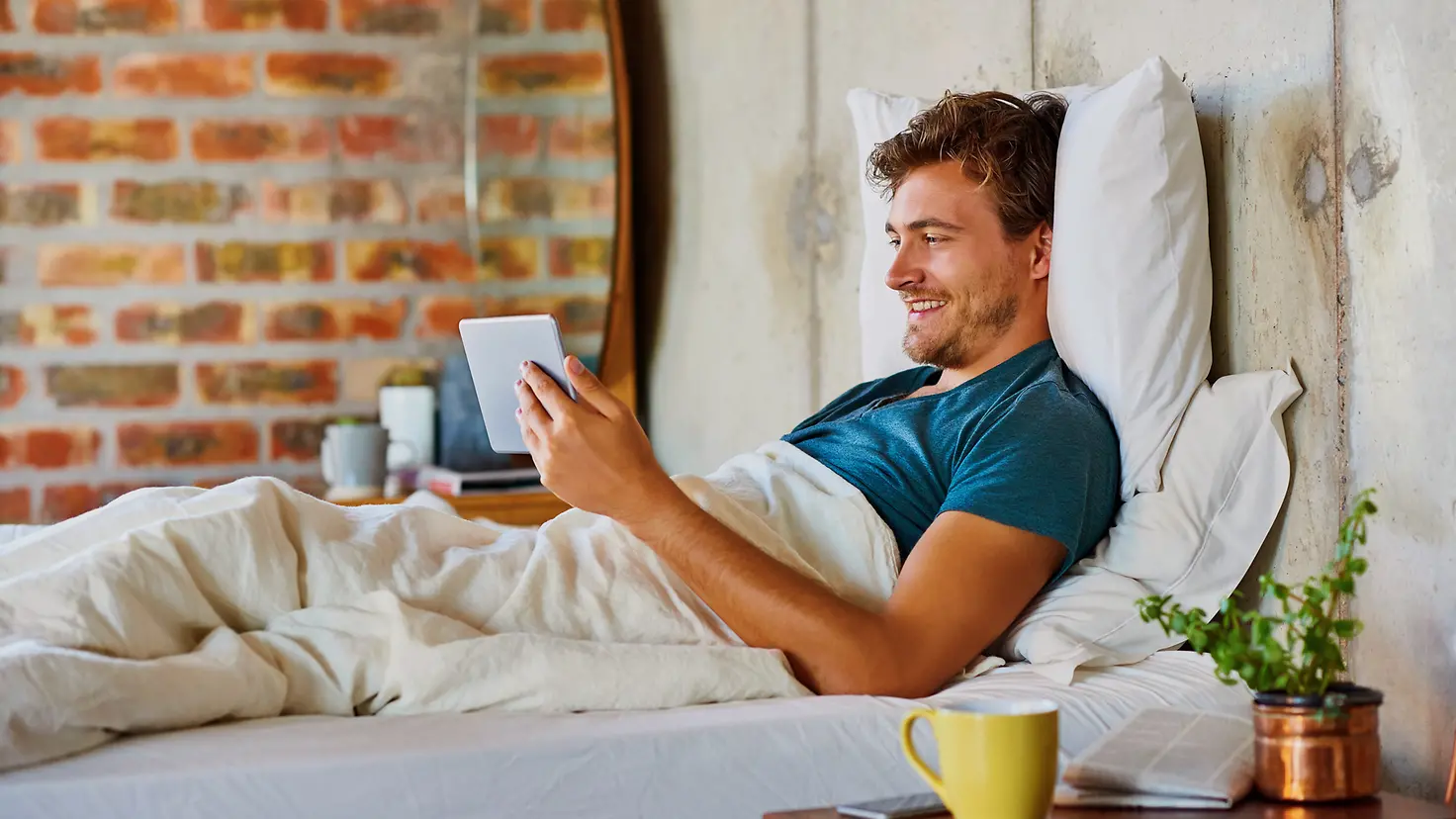 Ein Mann liegt mit einen Tablet im Bett