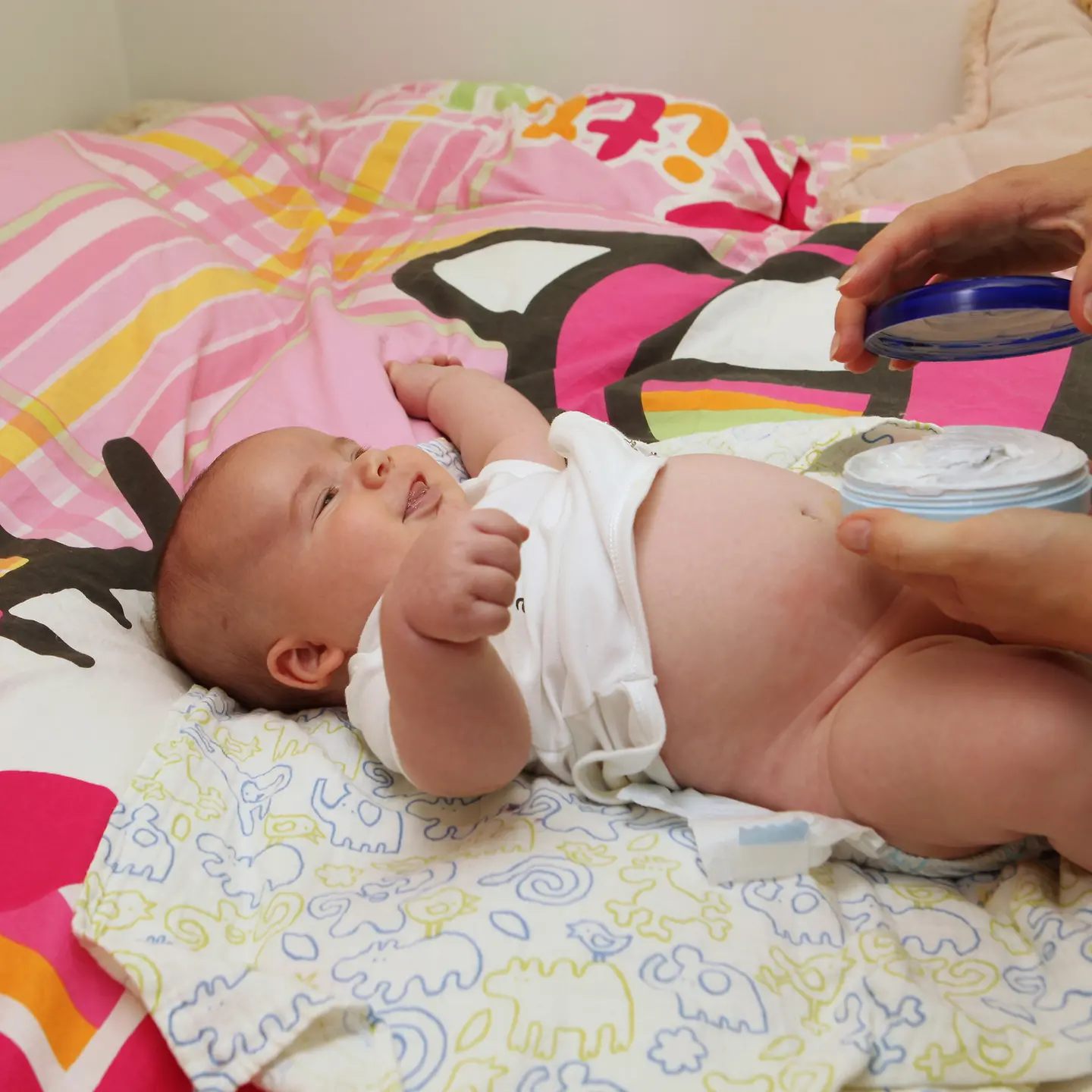Ein Baby liegt auf einer Decke und wird eingecremt.