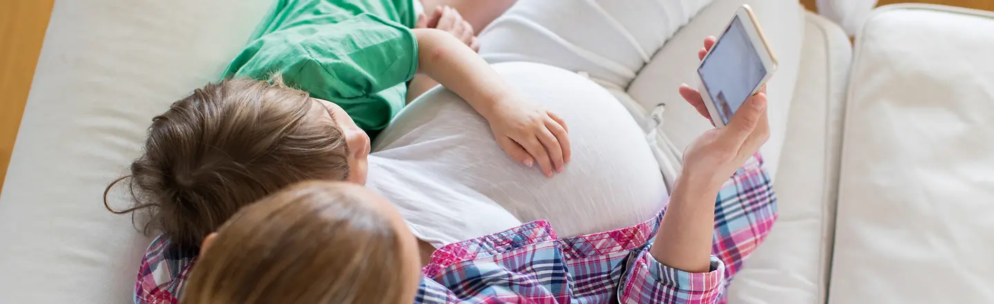 Eine schwangere Frau sitzt mit einem Kind auf einem Sofa