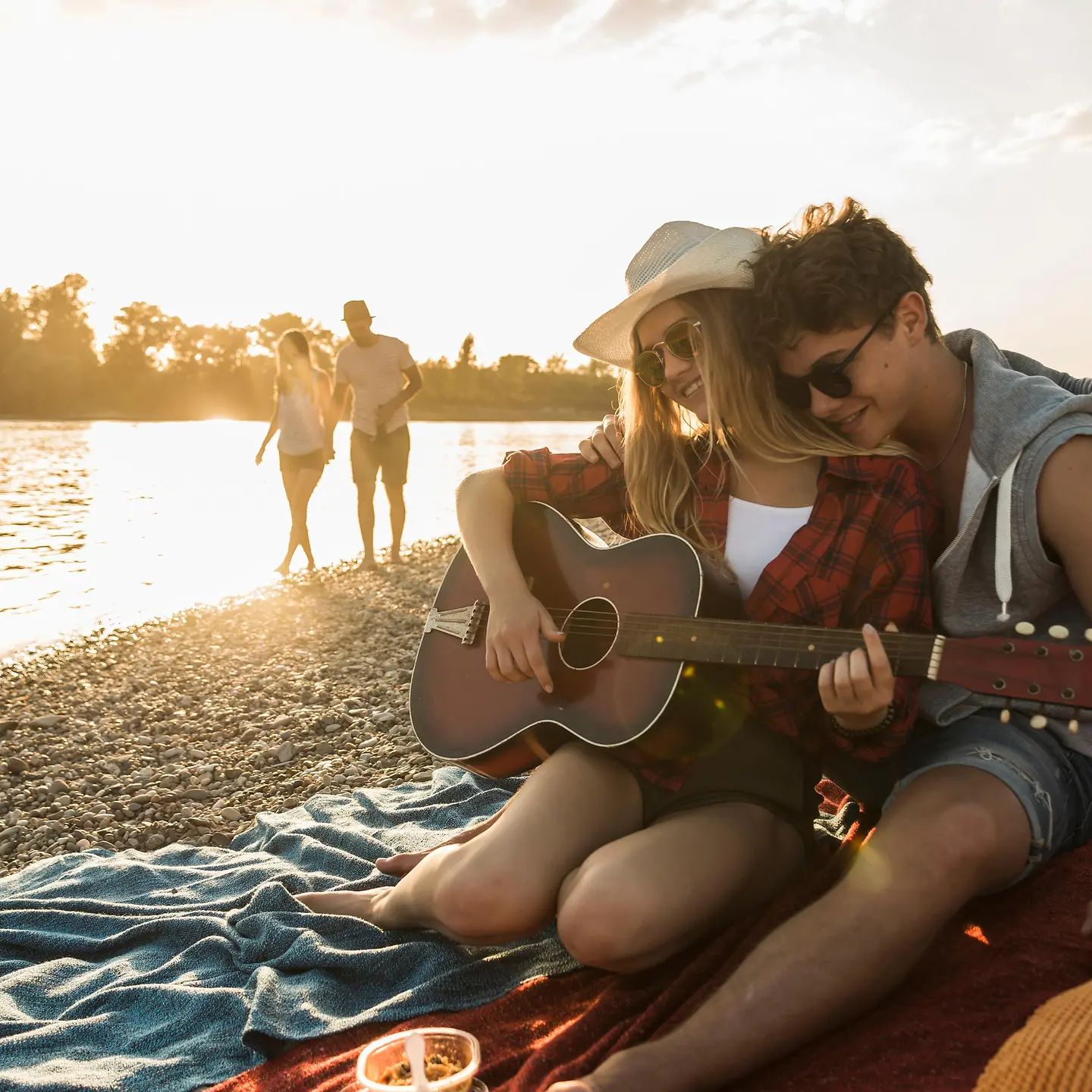Junges Paar sitzt mit einer Gitarre am Strand