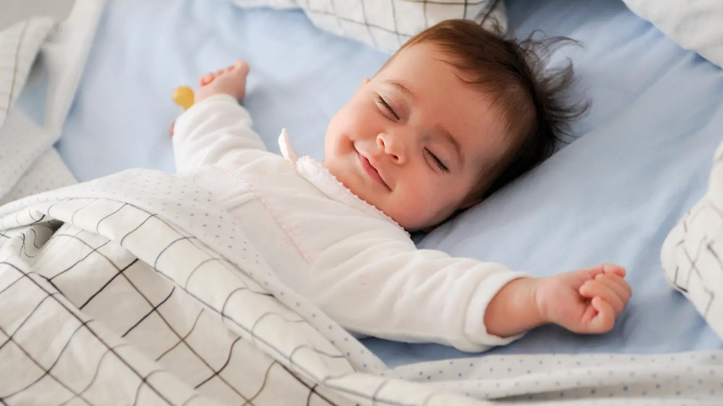 Ein Baby liegt in seinem Bett und lächelt im Schlaf