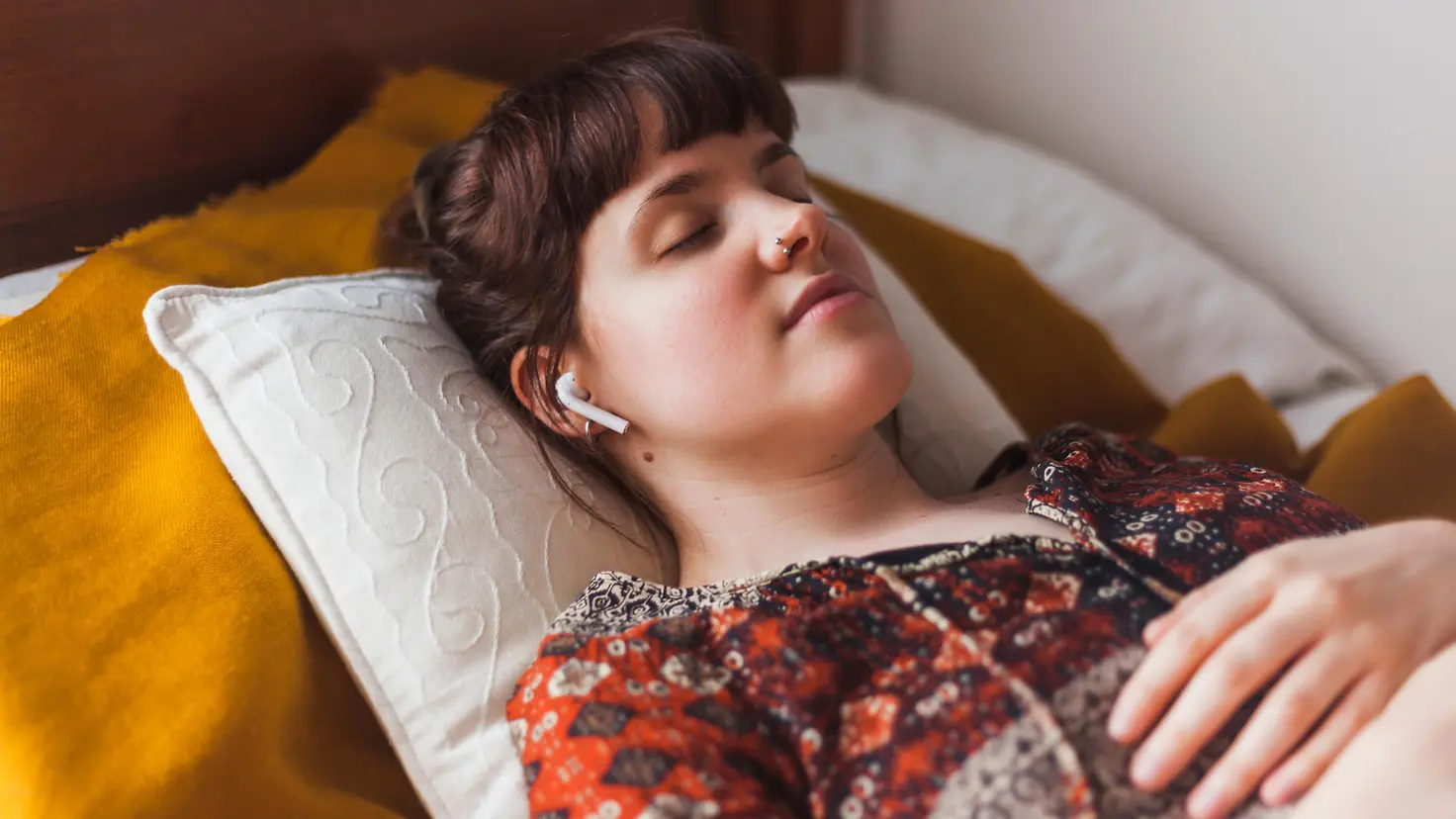 Eine Frau liegt mit Kopfhörern im Ohr schlafend im Bett