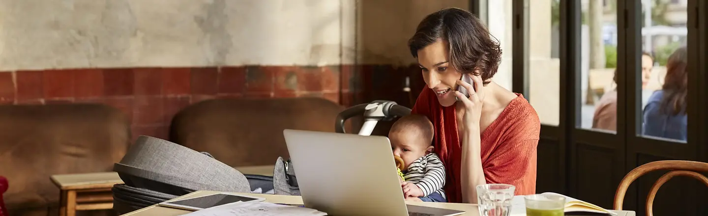 Eine Frau mit Laptop und Kind in einem Café.