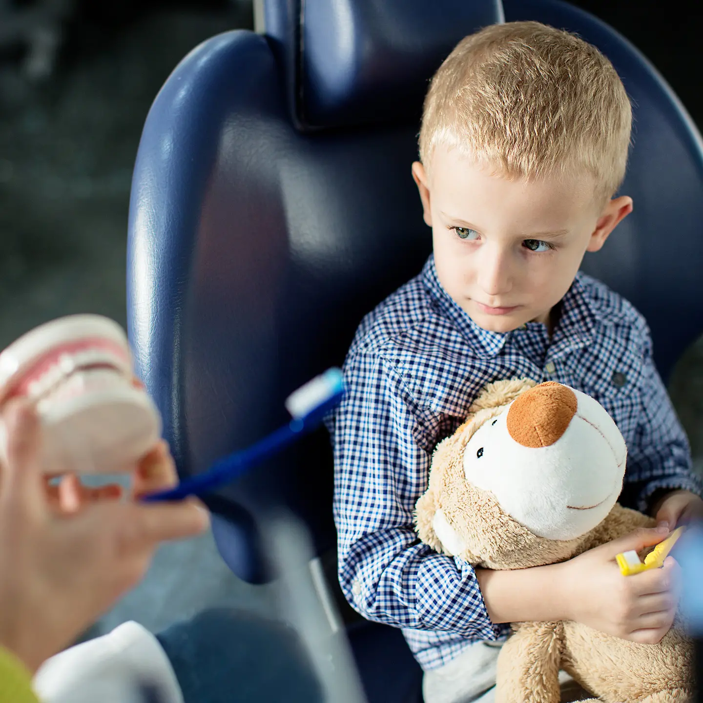 Ein kleiner Junge mit Teddy und Zahnbürste in der Hand beim Zahnarzt