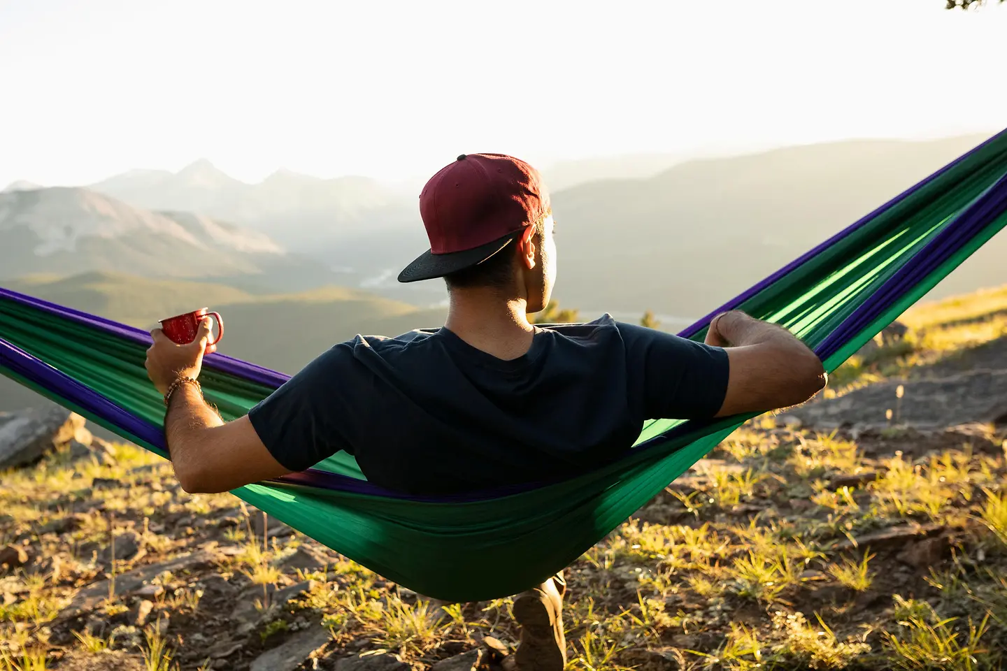 Ein Mann sitzt im Urlaub auf einer Hängematte und schaut in die Ferne.