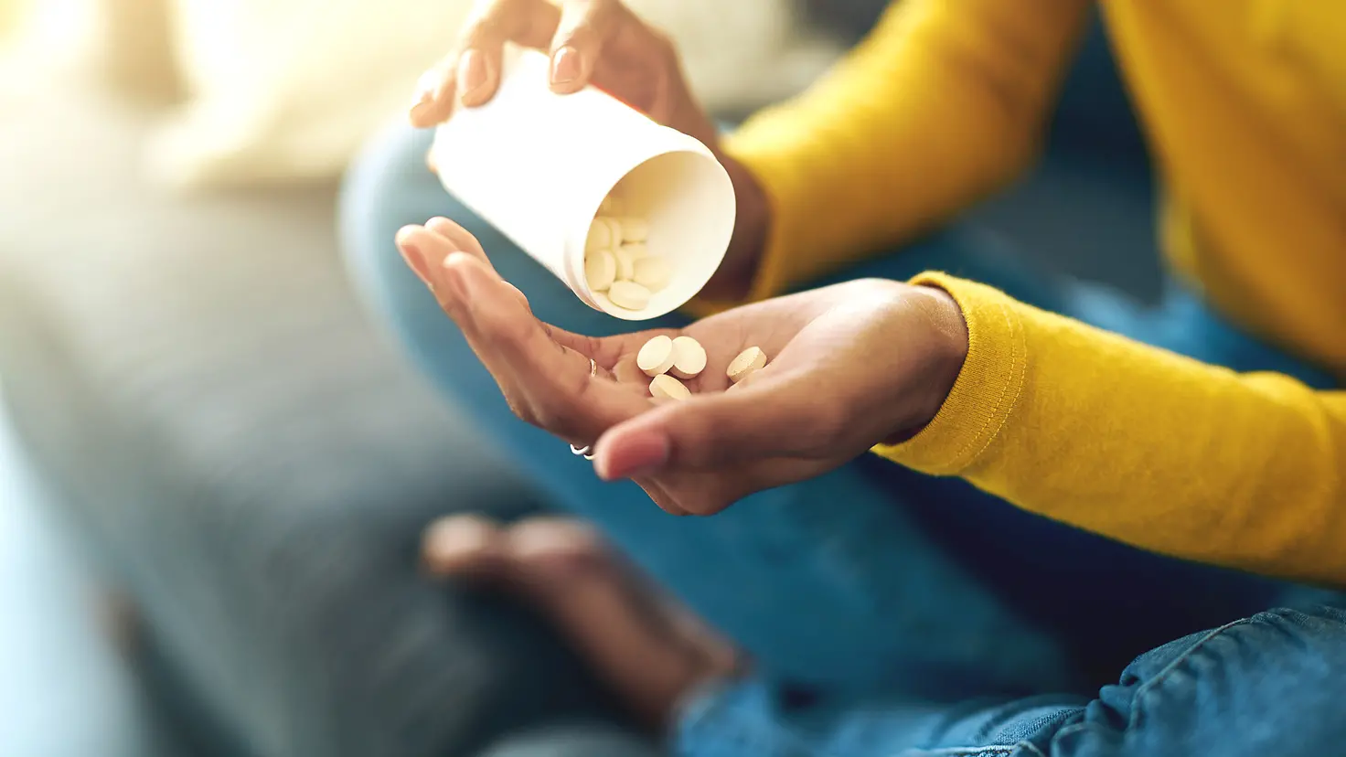 Eine Frau schüttet aus einem Behälter einige Tabletten in ihre linke Hand.