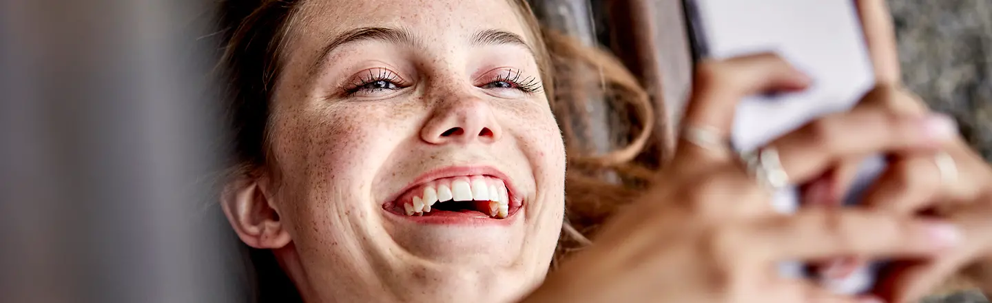 Junge Frau liegt lachend mit Smartphone auf dem Rücken