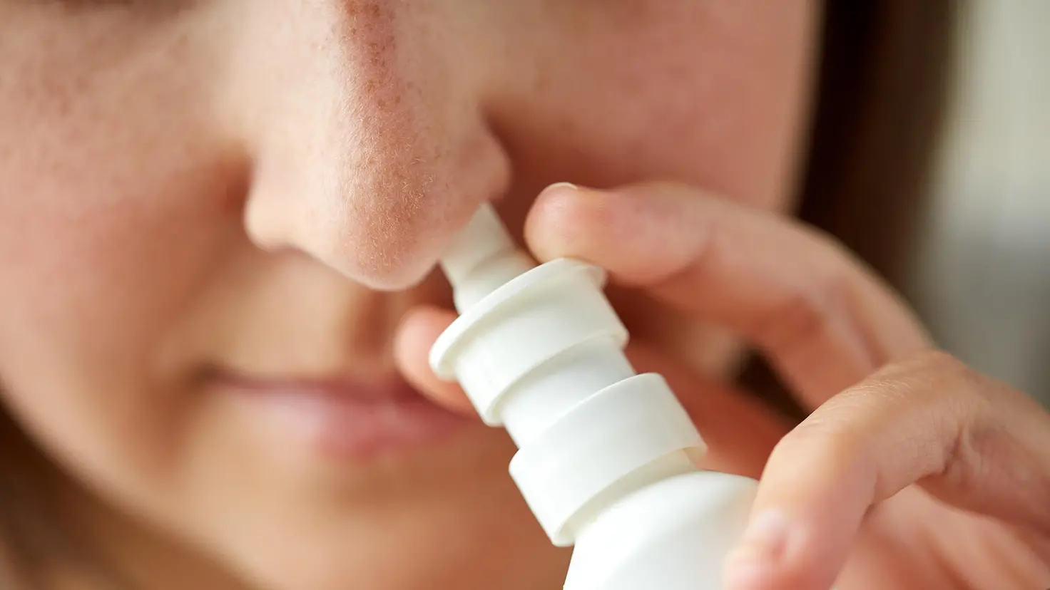 Eine junge Frau sprüht sich Nasenspray durch ein Nasenloch.