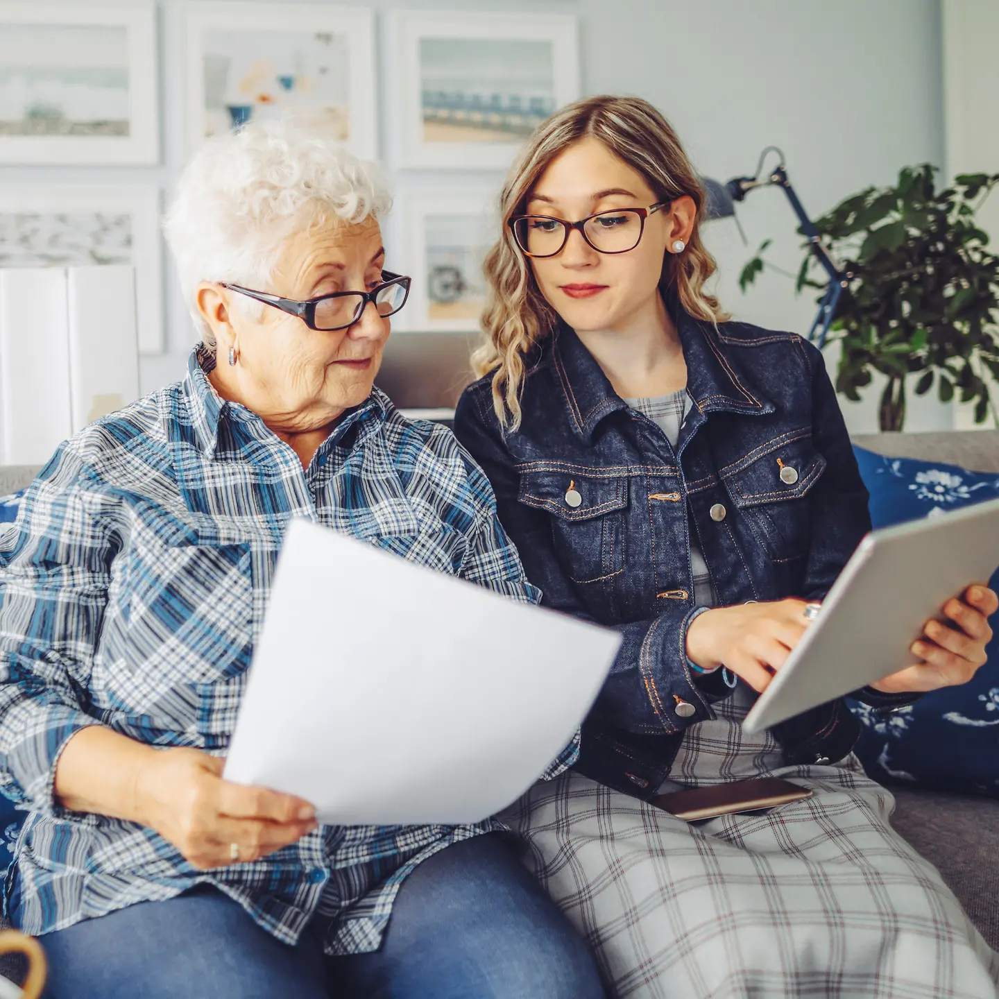 Großmutter und Enkelin sitzen auf dem Sofa und schauen sich Unterlagen an