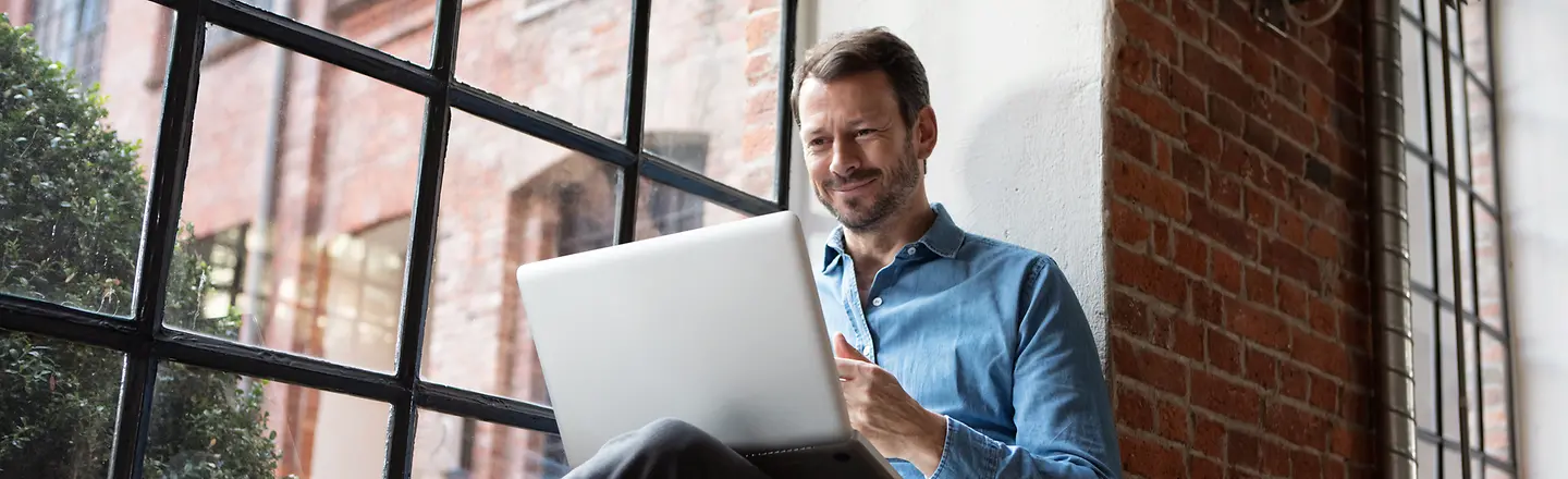 Ein Mann sitzt auf einer Fensterbank und nutzt einen Laptop